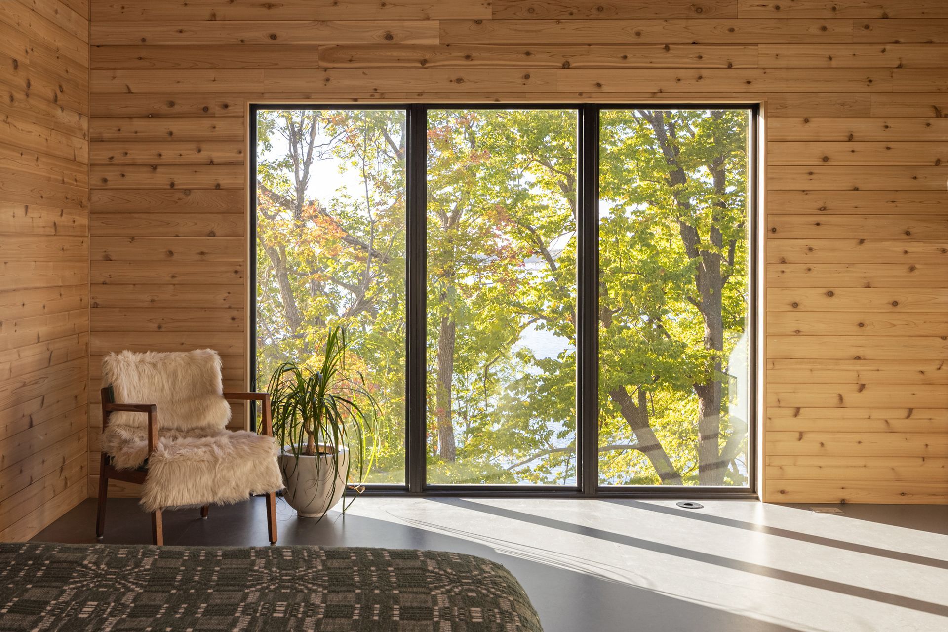 Cozy room with wood paneling, large windows overlooking fall foliage, and a comfortable armchair.