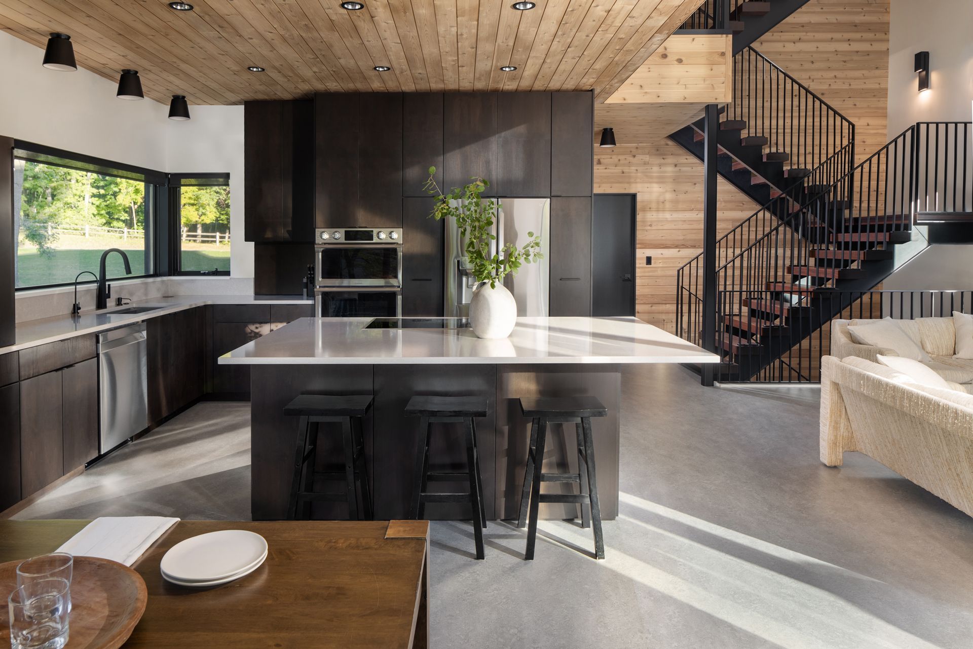 Modern kitchen with dark cabinetry, island with stools, and spiral staircase.