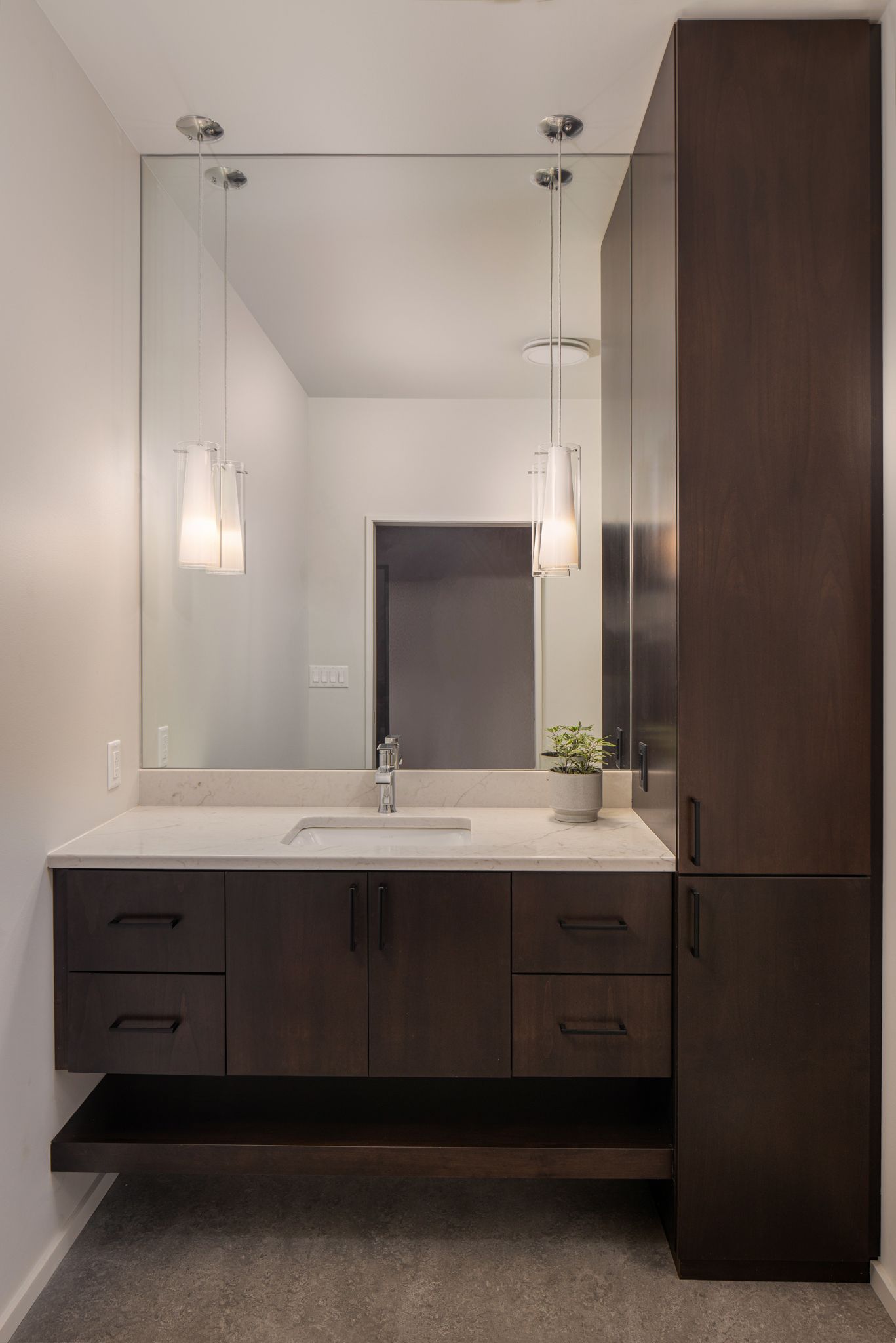 Modern bathroom with a large mirror, dark wood vanity and cabinet, and white countertop.