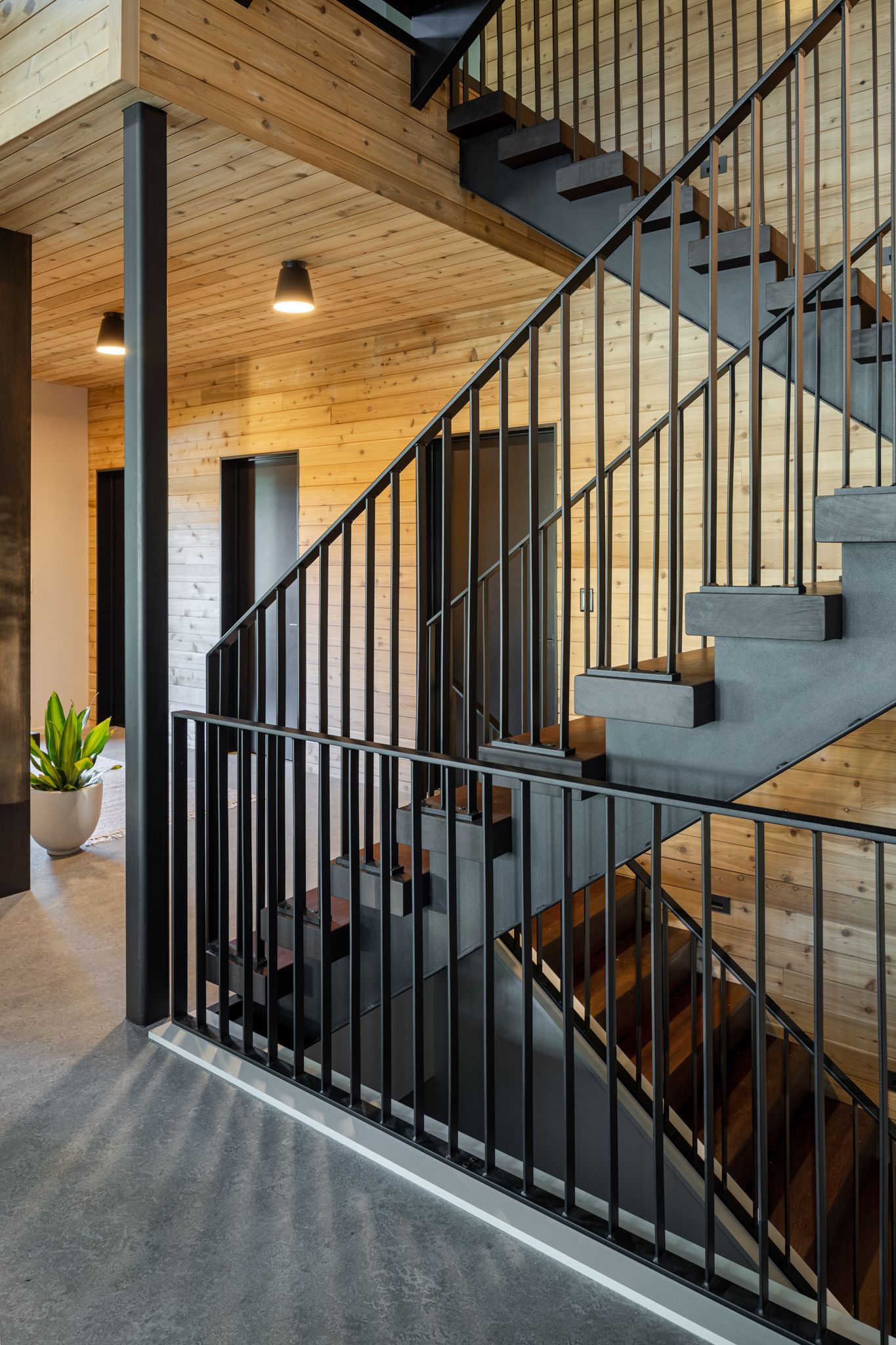 Staircase with black railing and gray steps in a building with wood paneling.