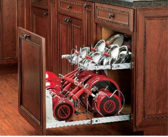 Pull-out kitchen cabinet with red and silver pots and pans stored in racks. Wooden cabinets are brown.