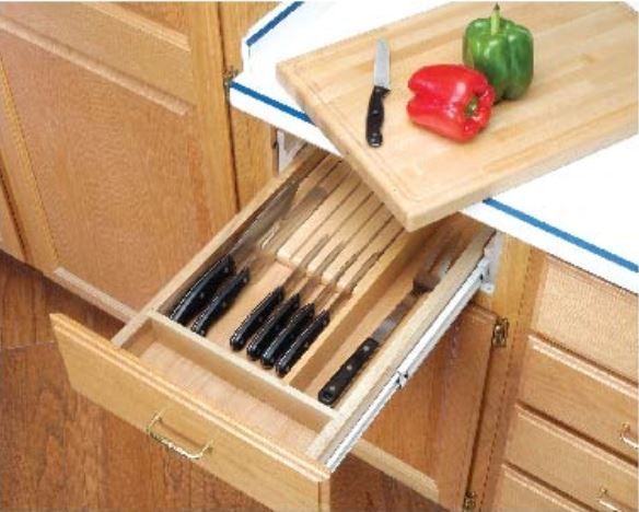 Wooden kitchen drawer with knives, open. A cutting board with peppers sits on the counter above.