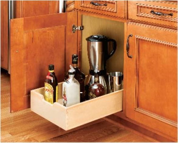 Pull-out drawer in a kitchen cabinet with bottles and a blender. Wooden cabinet, interior is beige.