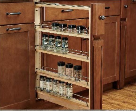 Pull-out spice rack in a kitchen cabinet, filled with spice jars. Brown wood and stainless steel.