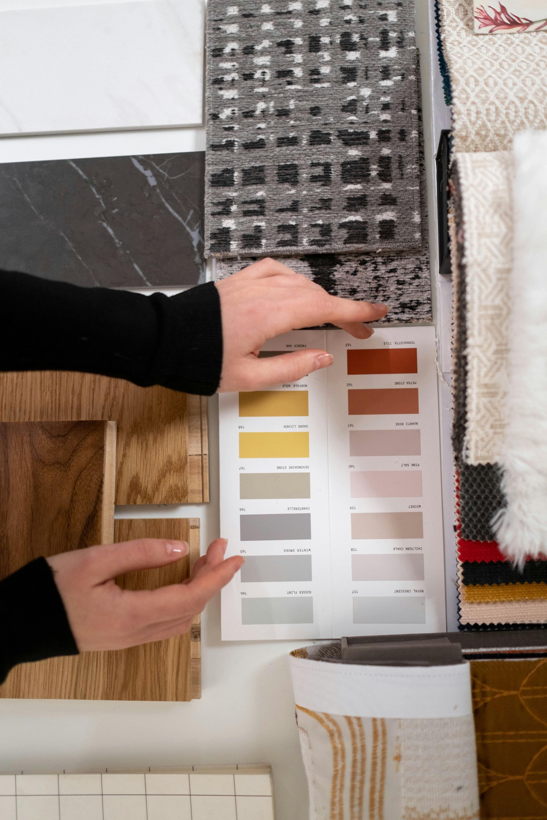 Hands pointing at a paint color swatch surrounded by fabric and material samples for interior design.