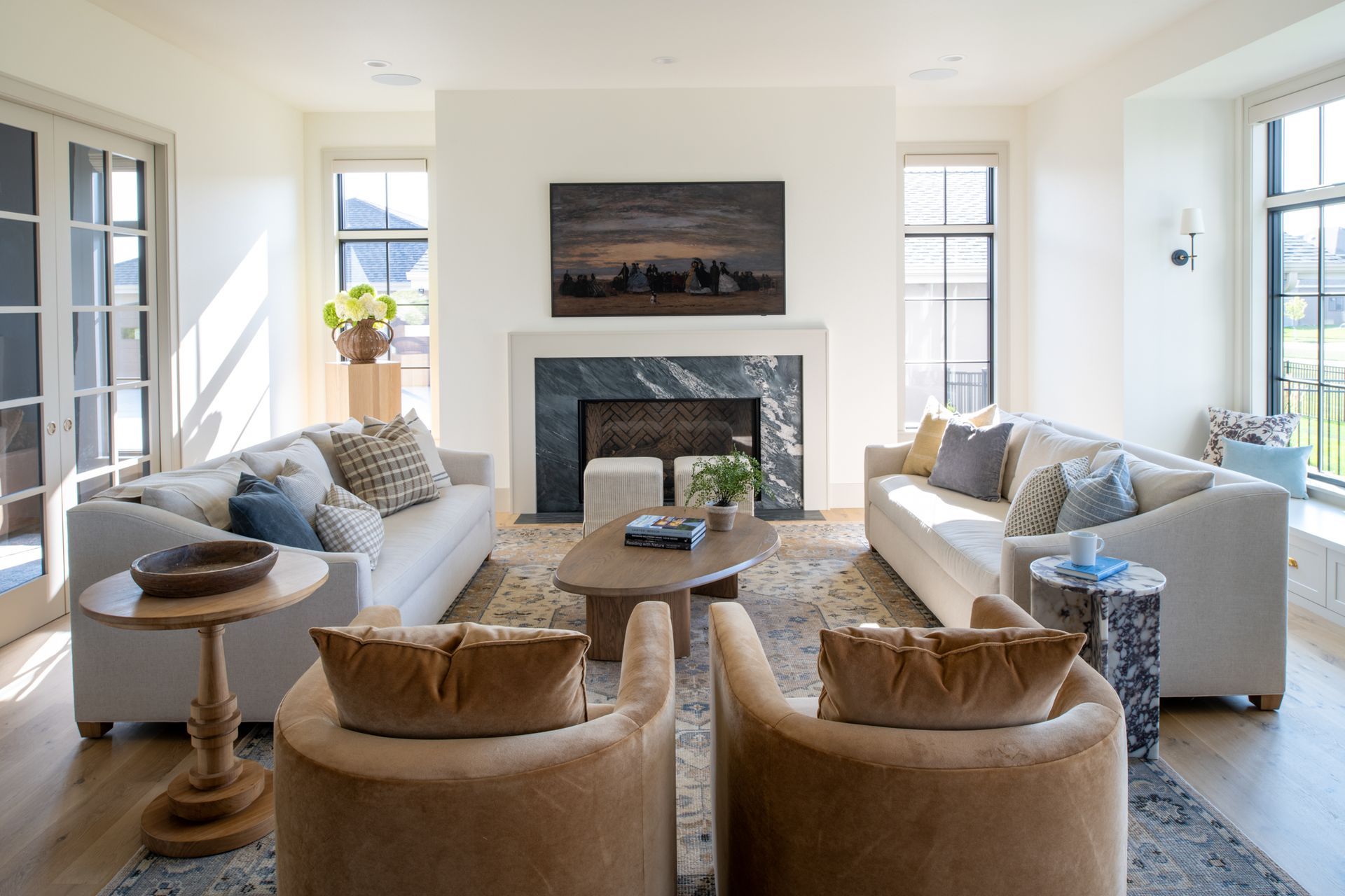 Living room with beige couches, two brown chairs, fireplace, and artwork.