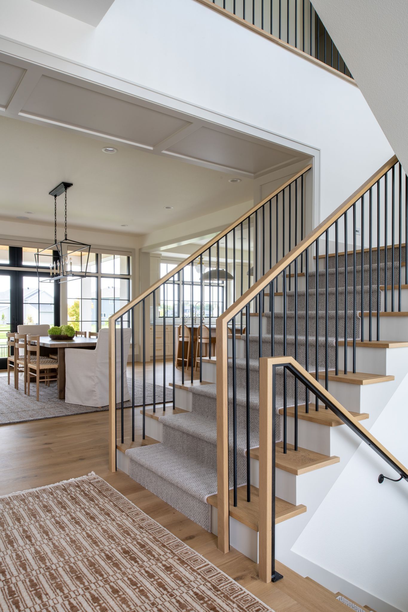Modern staircase with wood steps, black metal spindles, and light-colored wood railings.