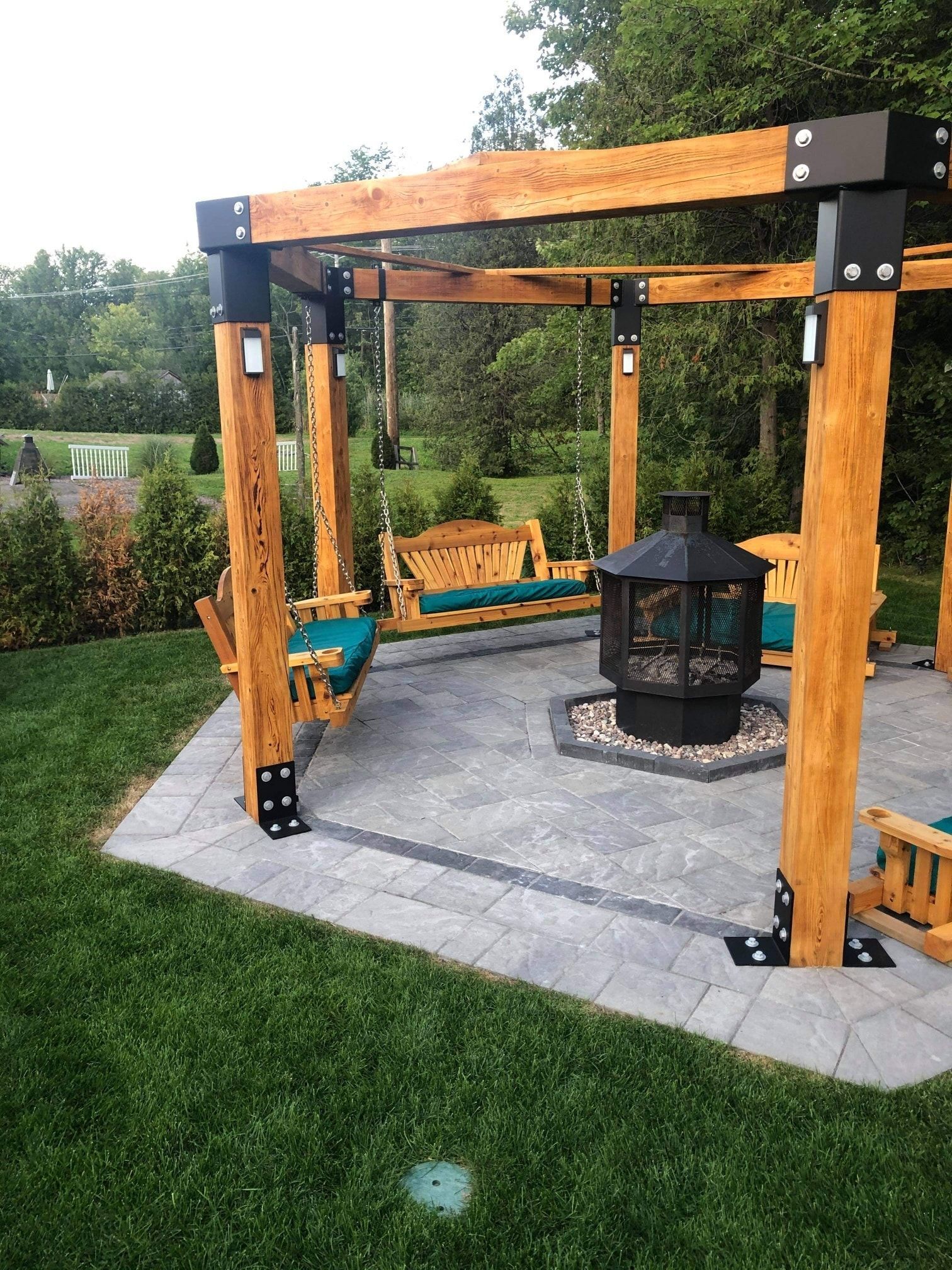 Une pergola en bois avec un foyer et des balançoires dans une cour arrière.