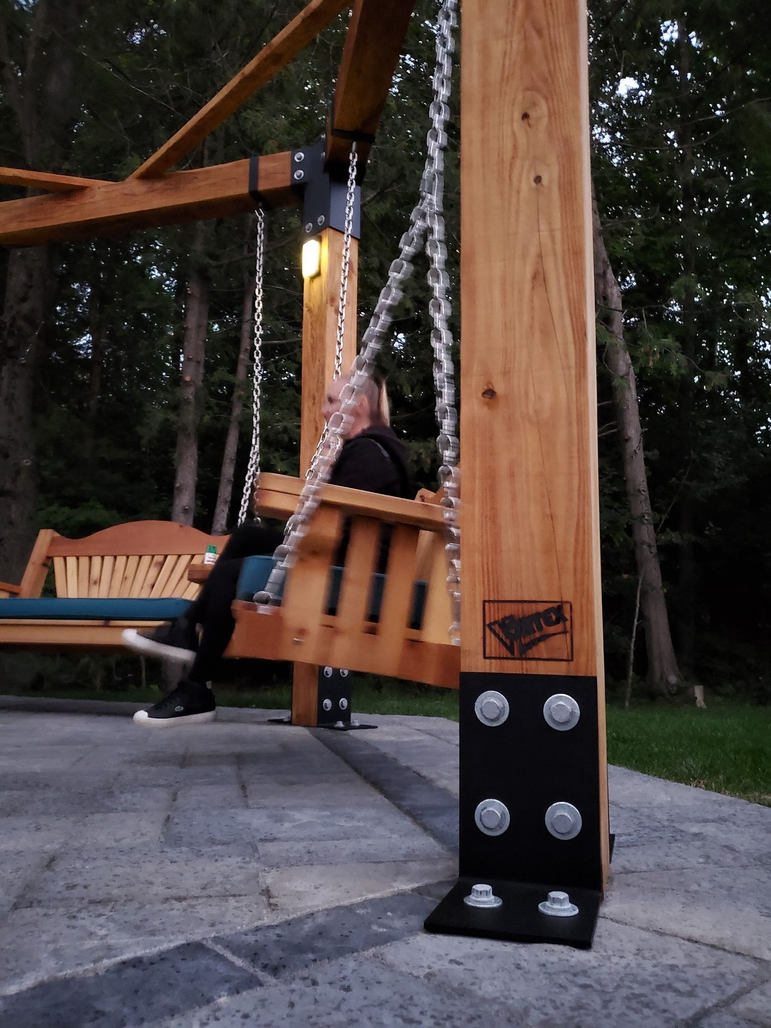Un homme est assis sur une balançoire en bois sous une pergola.