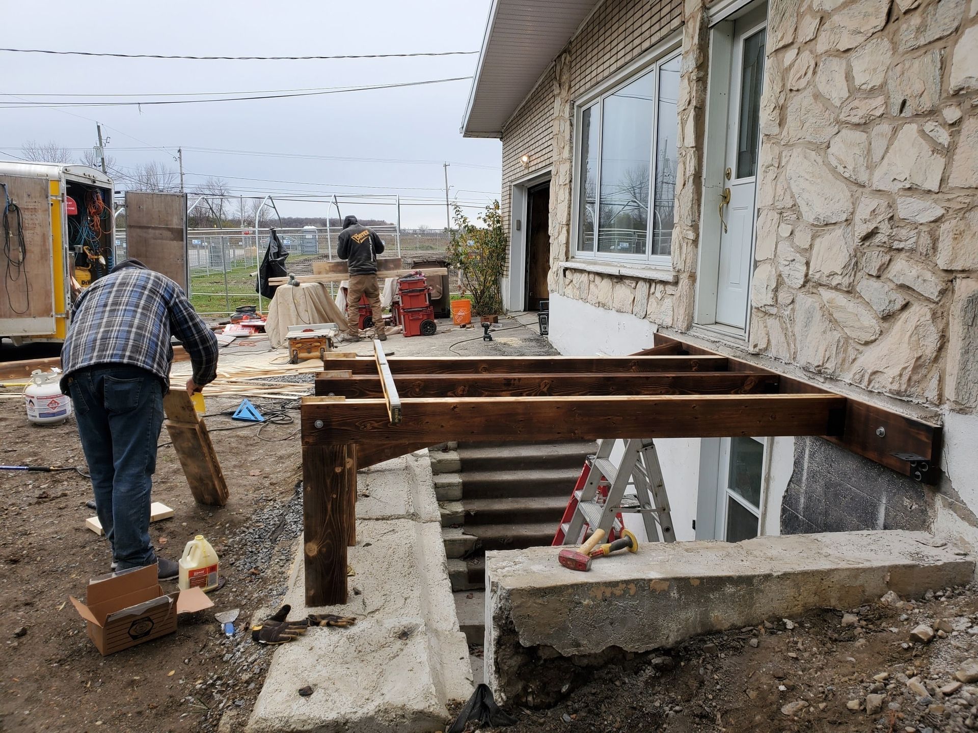 Un homme travaille sur une terrasse en bois devant une maison en pierre.
