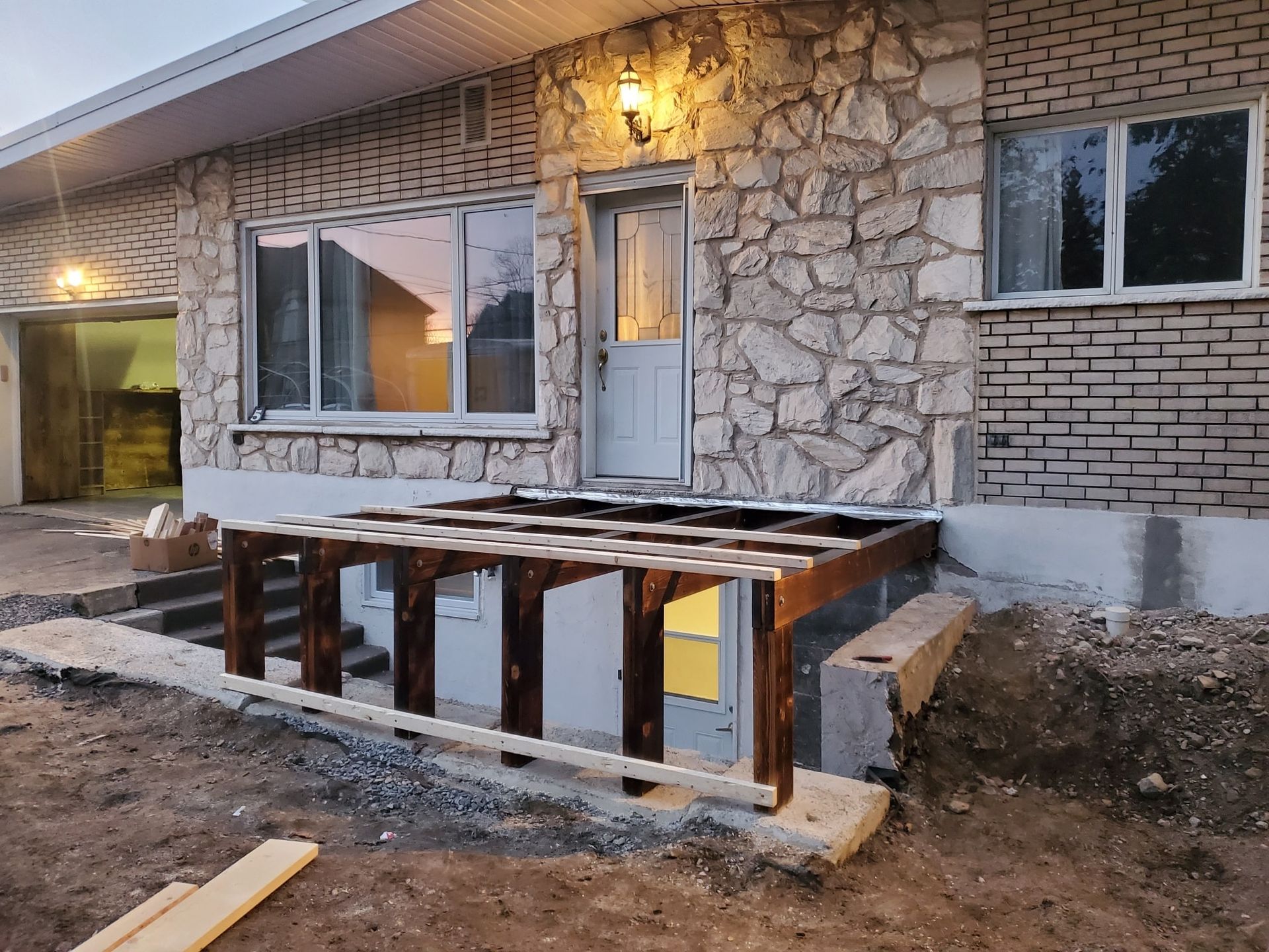Une terrasse en bois est en cours de construction devant une maison en briques.