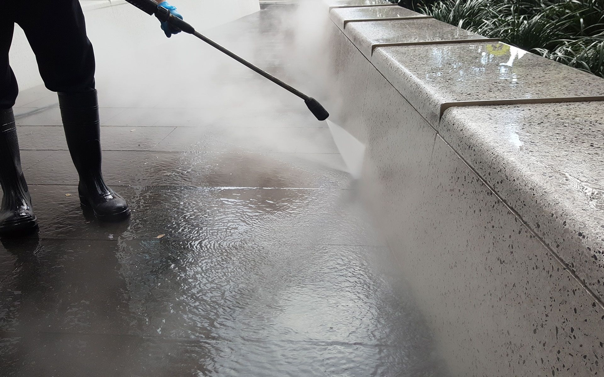 A person is using a high pressure washer to clean a sidewalk.