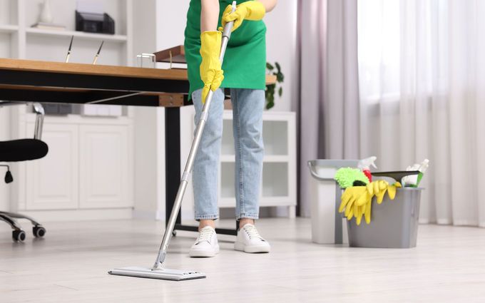 A woman is cleaning the floor with a mop in an office.