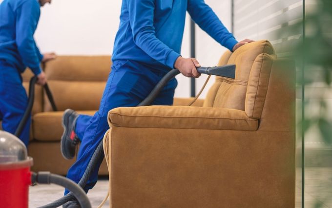 Two men are cleaning a couch with a vacuum cleaner.