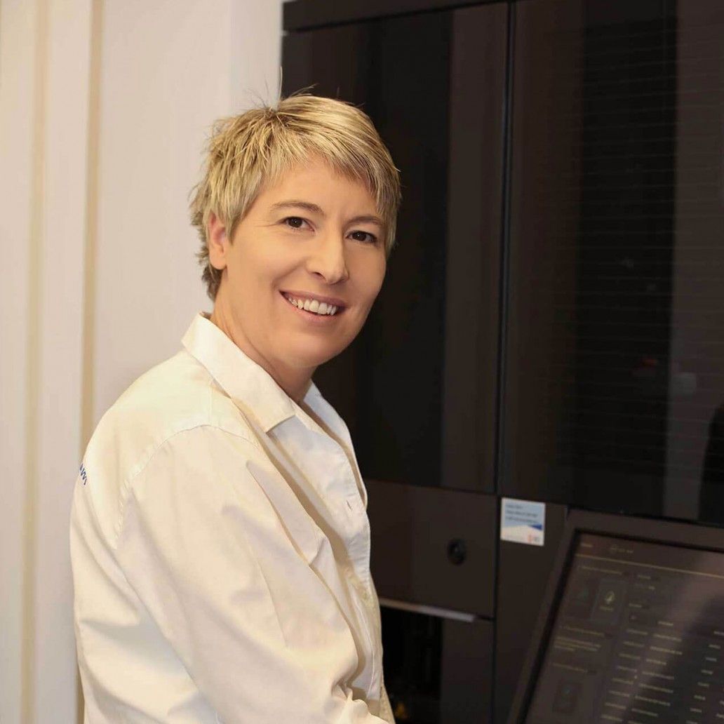 Eine Frau in einem weißen Hemd lächelt vor einem Computerbildschirm.