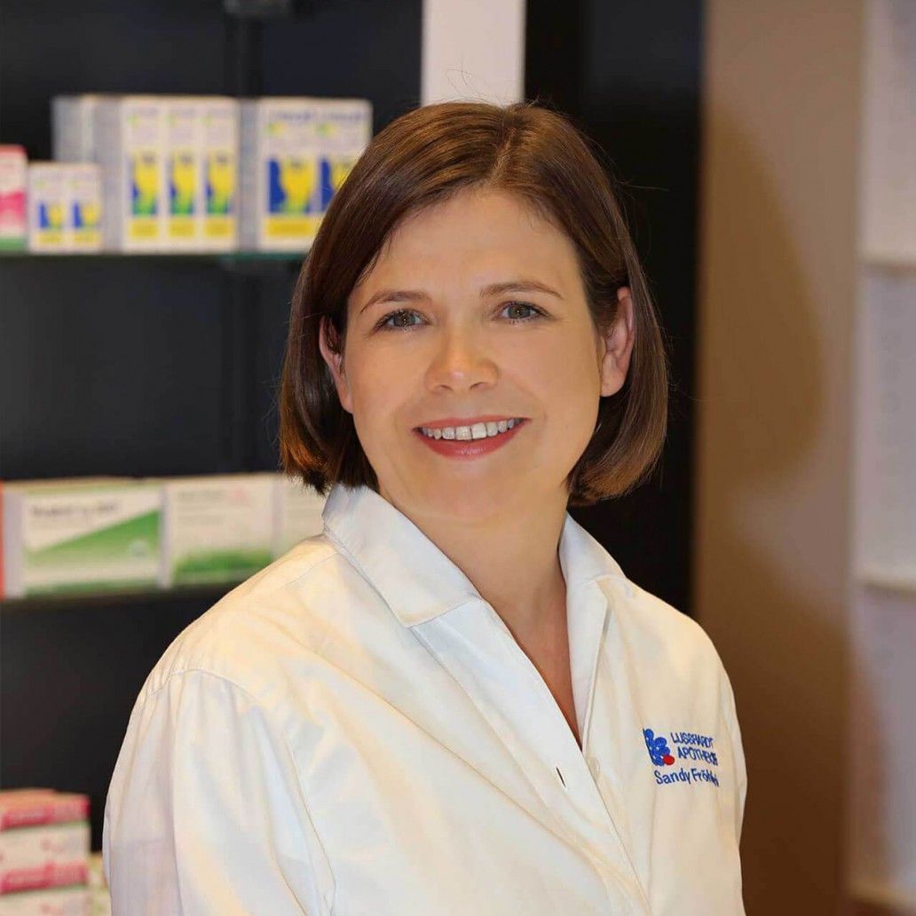 Eine Frau in einem weißen Laborkittel lächelt in einer Apotheke.