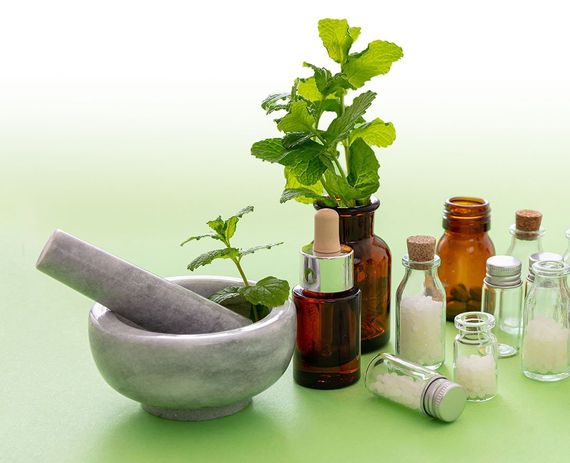 Ein Mörser und Stößel, umgeben von Flaschen und Pflanzen auf einem grünen Tisch.