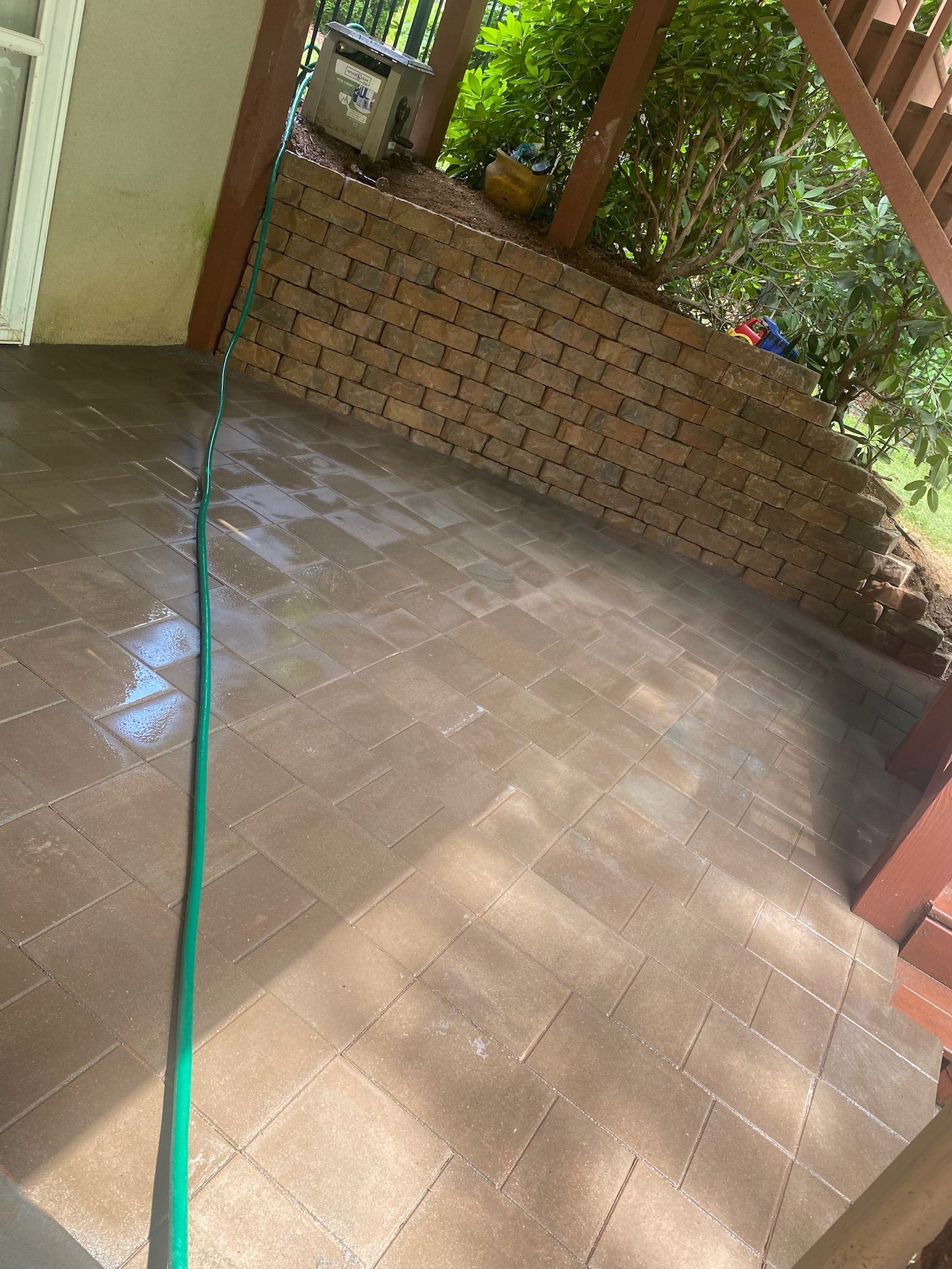 A green hose is connected to a brick wall on a patio.