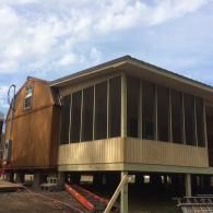 A wood-sided cabin with a large, elevated screened-in porch on a clear, partly cloudy day.