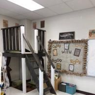 A lofted reading area with a ladder in a classroom, beside a 