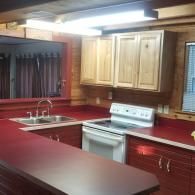 A kitchen with wood-paneled walls, reddish countertops, light wood cabinets, and a white stove.