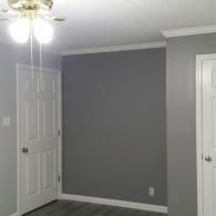 A room with a gray accent wall, two white doors, white trim, and a ceiling fan with light fixtures.