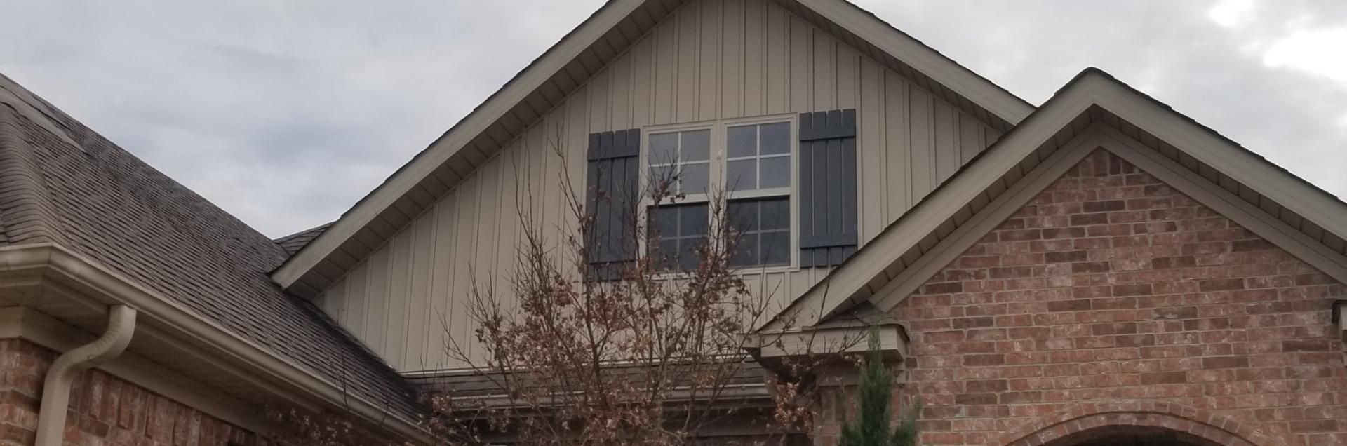 An exterior view of a brick house featuring a tan gabled dormer with a double window and dark shutters.