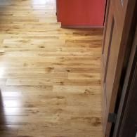 A high-angle view of glossy, light-brown hardwood flooring extending into a room near a partially open wooden door.
