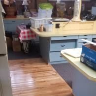 A light-colored office desk with blue drawers and an adjacent table with a red and white checkered cloth in a room.