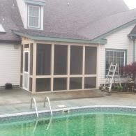 A beige screened-in porch addition attached to the back of a house next to an outdoor swimming pool.