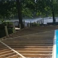 Wooden deck frame under construction next to a swimming pool, overlooking a body of water and trees.