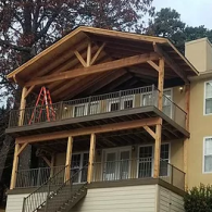A two-story house with a wooden deck and covered porch featuring a timber-framed roof structure, with an orange ladder.
