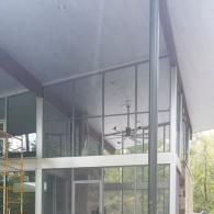 A modern structure with floor-to-ceiling glass walls, a prominent gray steel post, and a ceiling fan visible inside.