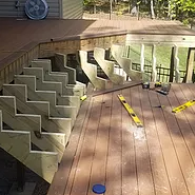 Several wooden stair stringers are installed on the edge of a brown composite deck under construction.