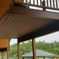 Low-angle view of a brown slatted outdoor deck ceiling overlooking a lake with a small green-roofed gazebo.