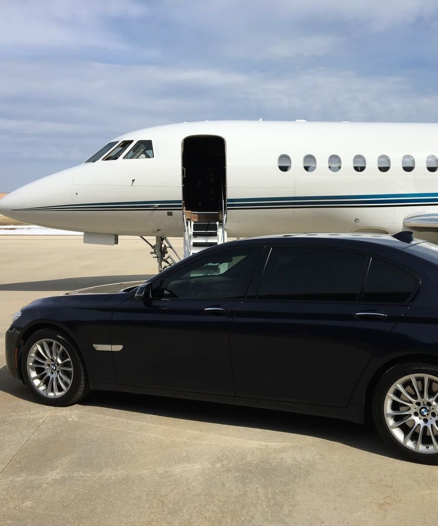 A black car is parked in front of a private jet