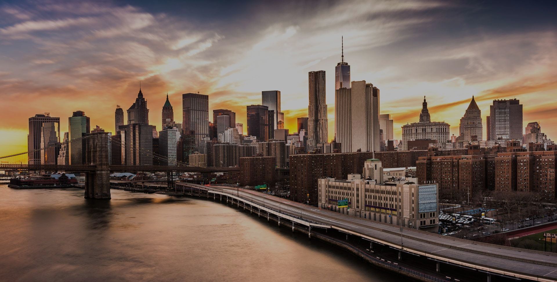 A city skyline at sunset with a bridge in the foreground.