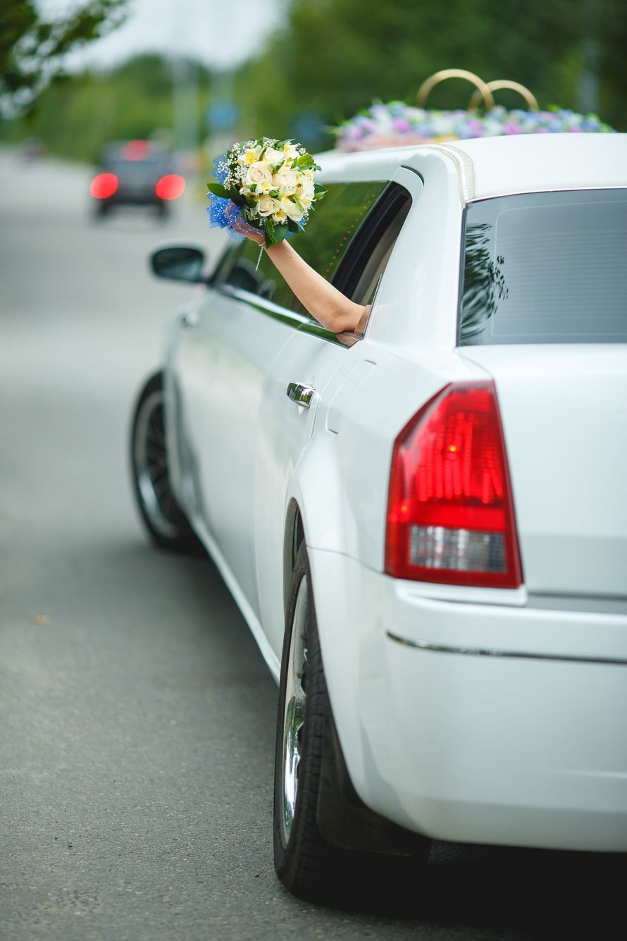 A bride is holding a bouquet of flowers out of the window of a white limousine.