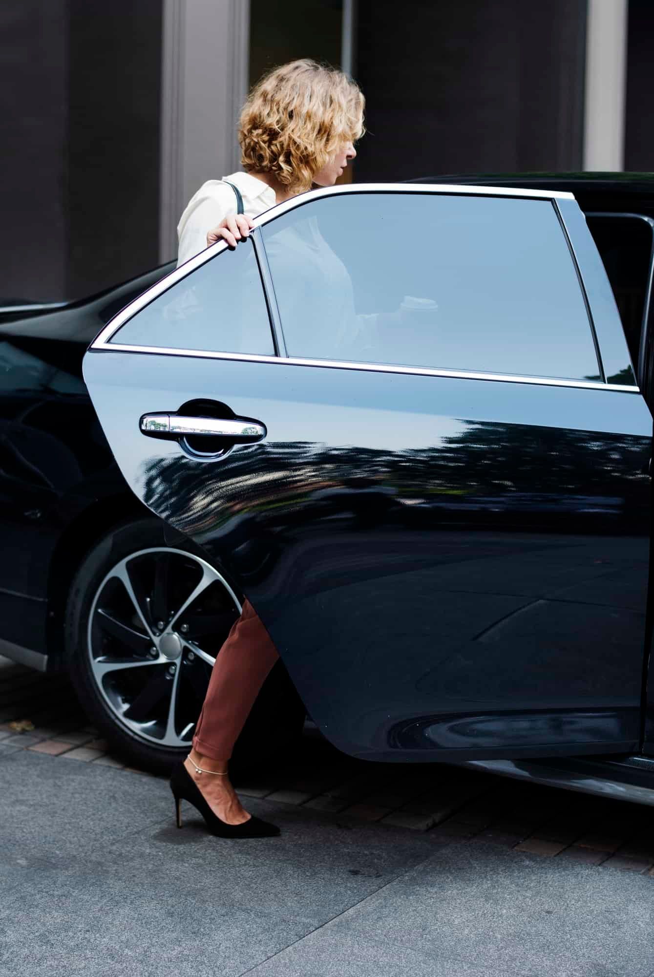 A woman is getting out of a black car.