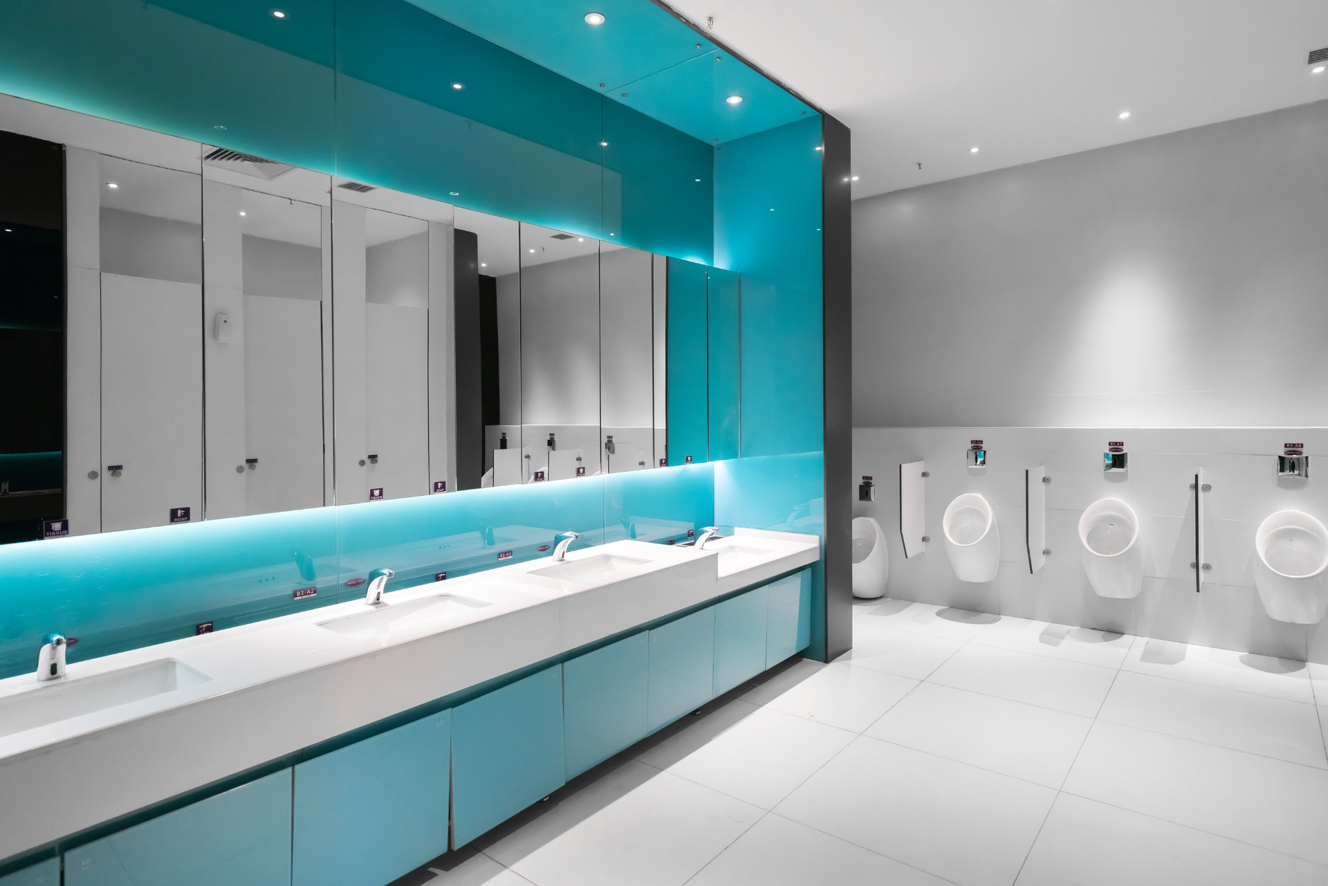 Toilettes publiques modernes aux touches de blanc et de turquoise. Urinoirs et lavabos visibles.