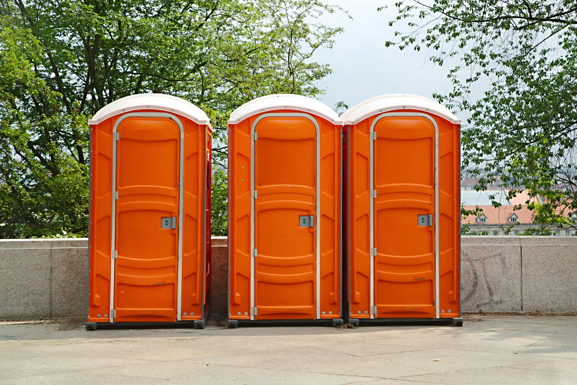 Trois toilettes portables orange dans un cadre extérieur.