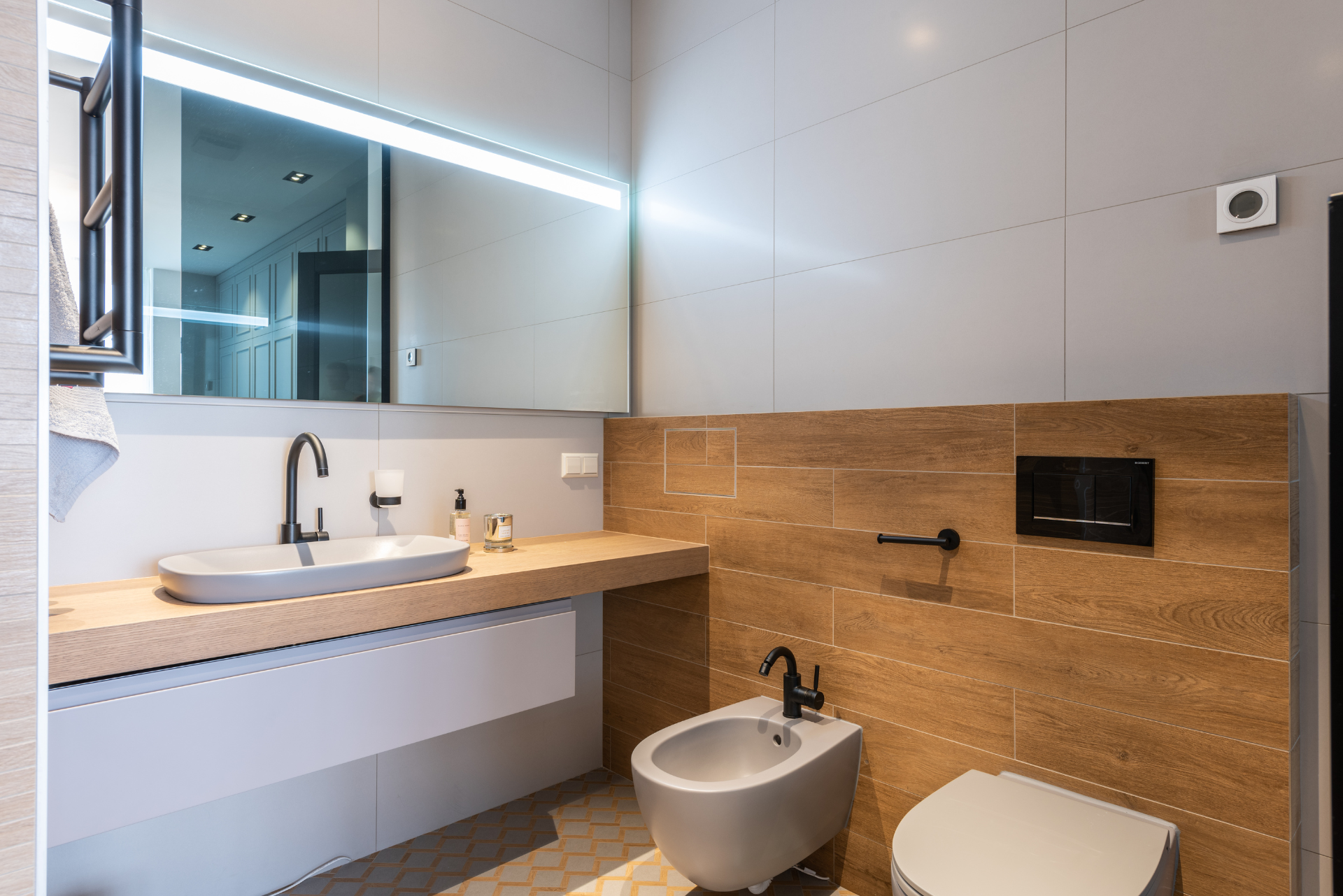 Salle de bain moderne avec mur d'accent en bois, lavabo blanc et bidet.