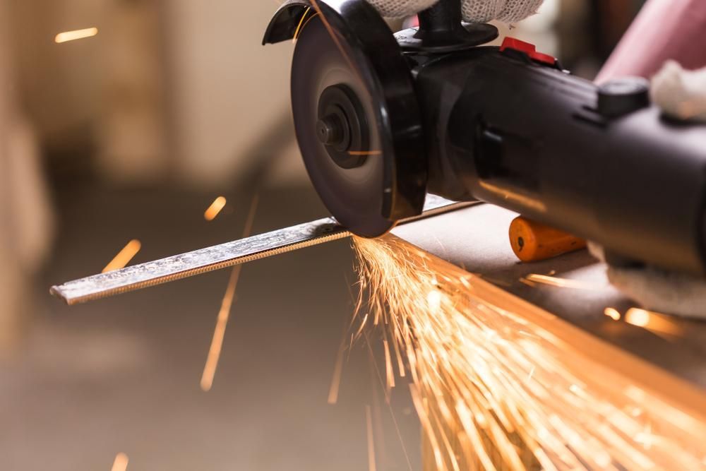 A Person Is Using a Grinder to Cut a Piece of Metal — Sheetmetal Improvements & Design Pty Ltd in Yatala, QLD