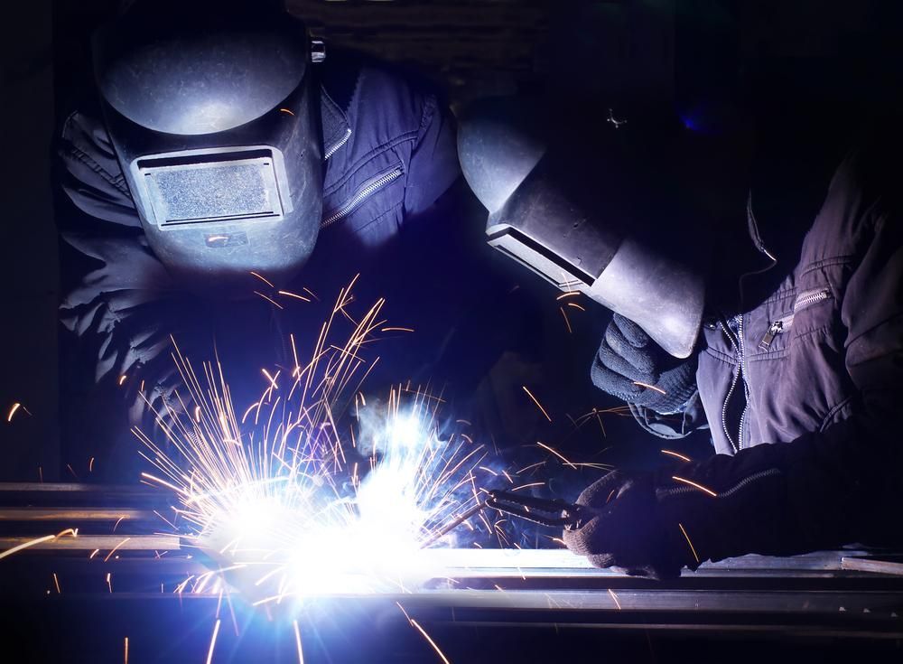 A Man Wearing a Welding Mask Is Welding a Piece of Metal — Sheetmetal Improvements & Design Pty Ltd in Southport, QLD