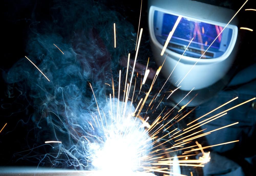 A Man Wearing a Welding Mask Is Welding a Piece of Metal — Sheetmetal Improvements & Design Pty Ltd in Tweed Heads, NSW