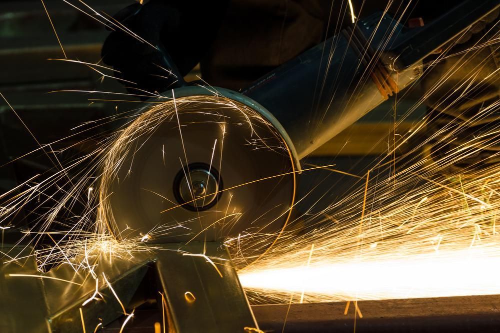 A Person Is Using a Grinder to Cut a Piece of Metal — Sheetmetal Improvements & Design Pty Ltd in Molendinar, QLD