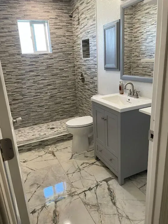A bathroom with a toilet , sink , mirror and walk in shower.