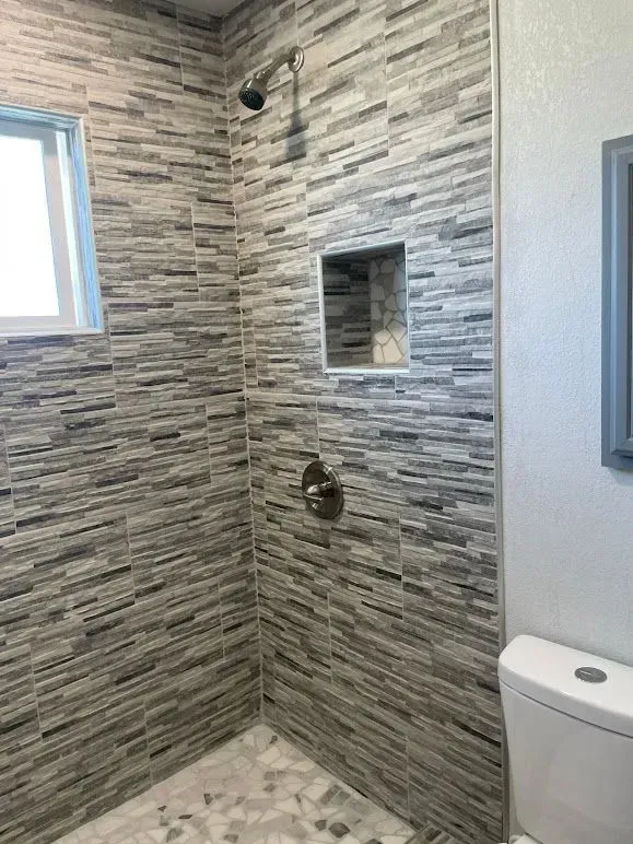 A bathroom with a shower , toilet and window.