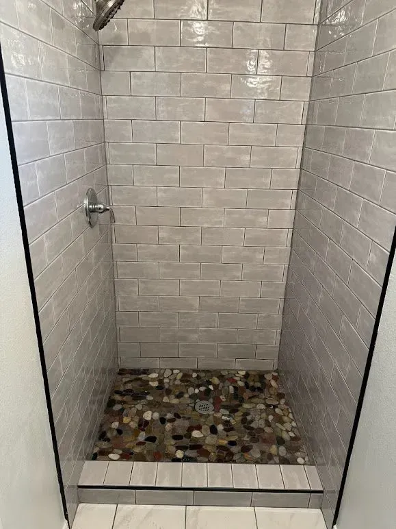 A shower with a tiled wall and a stone floor.