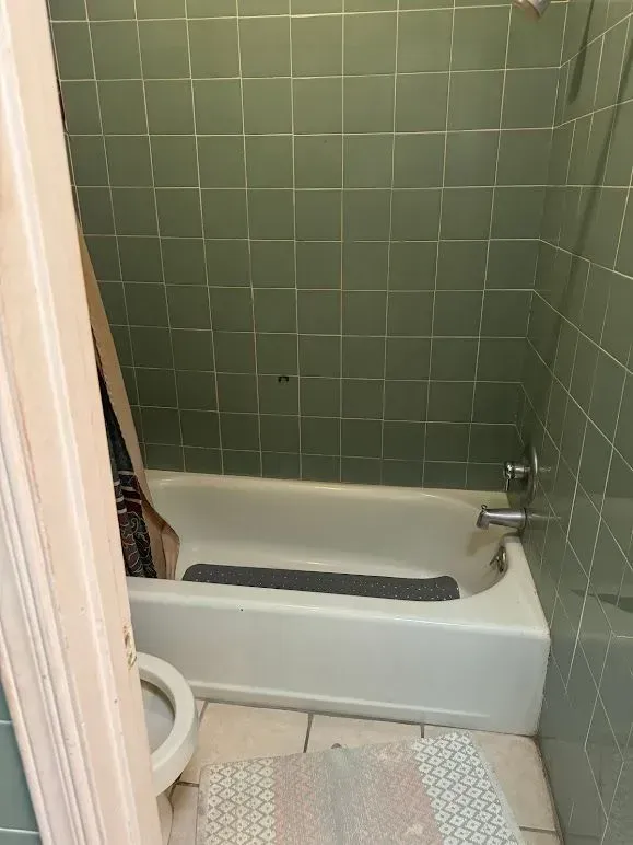 A bathroom with a bathtub , toilet , and green tiles.
